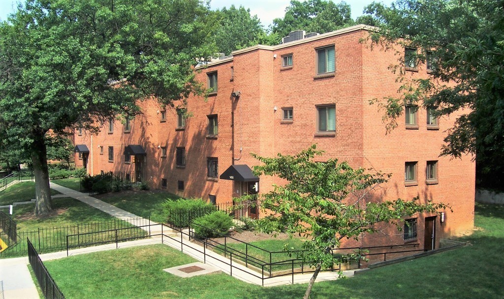 A red brick building with a black fence and trees in front.